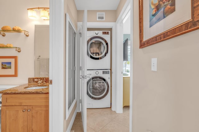 washroom with visible vents, a sink, light tile patterned flooring, stacked washer / drying machine, and laundry area