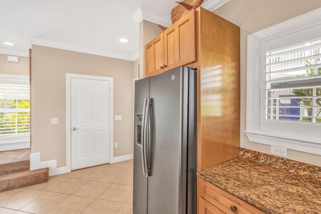 kitchen with crown molding, baseboards, stainless steel fridge with ice dispenser, light tile patterned floors, and dark stone countertops