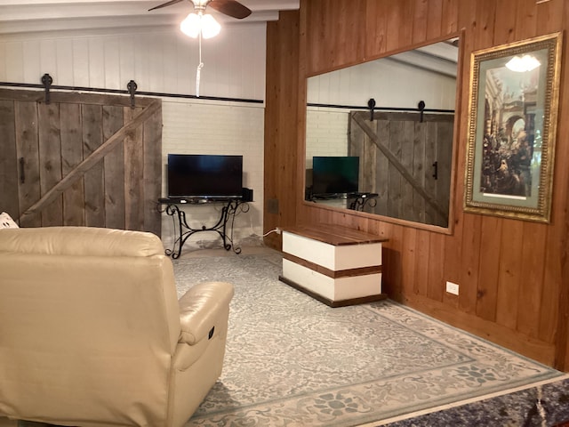 living area featuring a barn door, a ceiling fan, and wooden walls