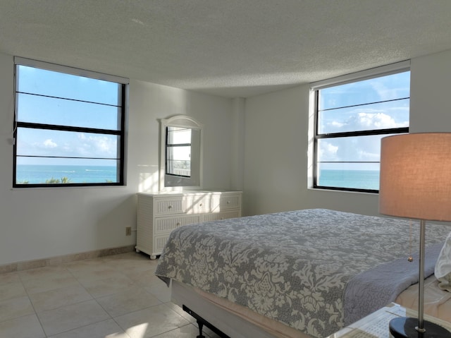 bedroom with a water view, light tile patterned floors, baseboards, and a textured ceiling