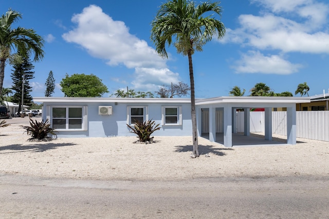 view of front facade featuring fence, an attached carport, stucco siding, and a wall mounted AC