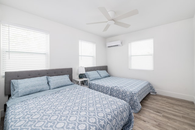 bedroom featuring an AC wall unit, baseboards, ceiling fan, and wood finished floors
