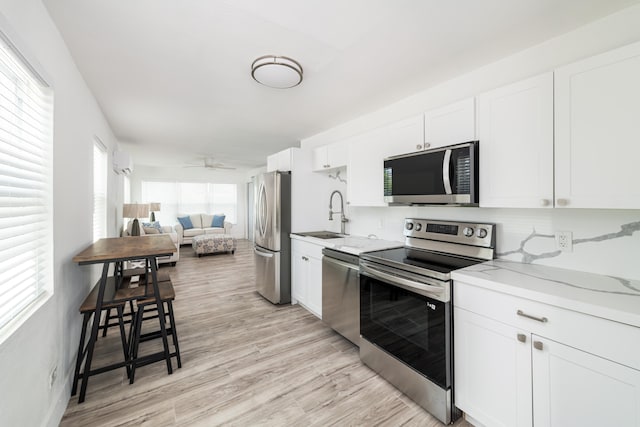kitchen with white cabinets, light stone counters, a sink, light wood-style floors, and stainless steel appliances