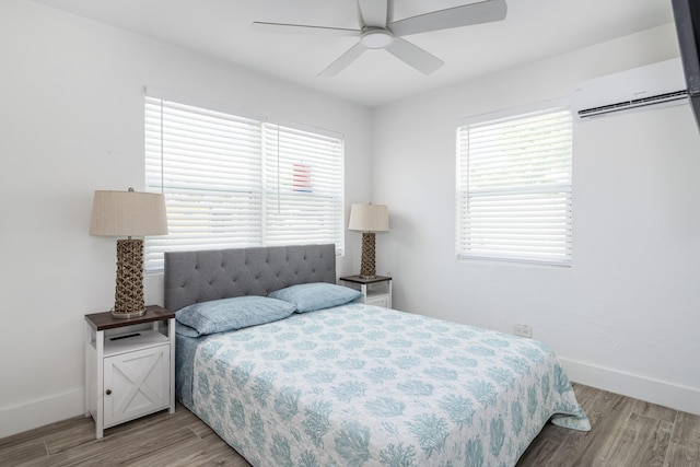 bedroom with baseboards, multiple windows, wood finished floors, and a wall mounted air conditioner