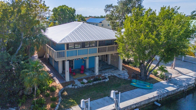 back of house with metal roof, a patio, a yard, and boat lift