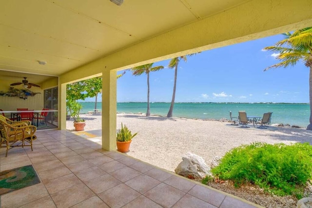 view of patio / terrace with outdoor dining area, a water view, ceiling fan, and a view of the beach