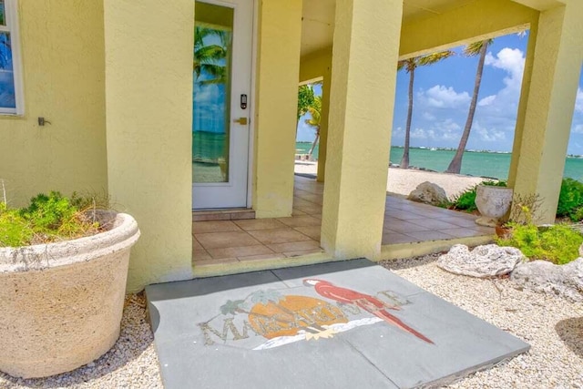 doorway to property featuring a water view, a patio, and stucco siding