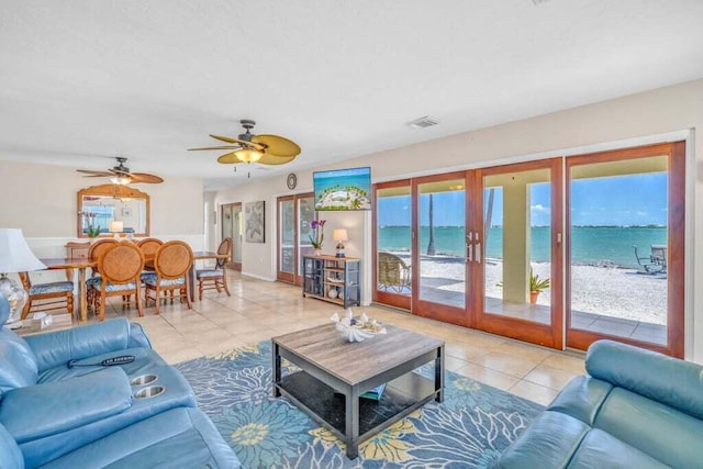 tiled living room featuring a water view, a ceiling fan, french doors, and visible vents