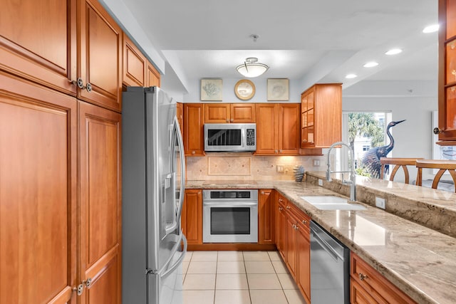 kitchen featuring decorative backsplash, light stone counters, brown cabinets, stainless steel appliances, and a sink