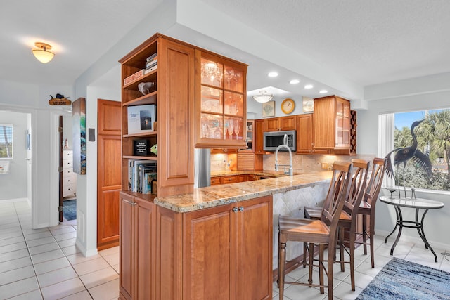 kitchen with brown cabinets, stainless steel microwave, glass insert cabinets, and a peninsula