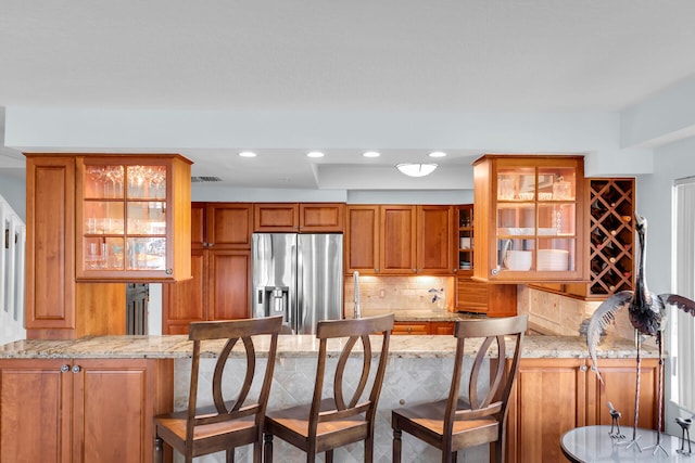 kitchen with a peninsula, stainless steel fridge, glass insert cabinets, and brown cabinetry