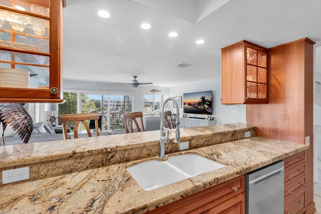 kitchen with brown cabinetry, glass insert cabinets, a sink, light stone countertops, and stainless steel dishwasher