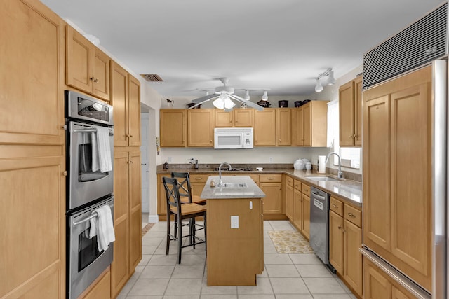 kitchen with stainless steel appliances, a sink, a kitchen island, a kitchen breakfast bar, and light countertops