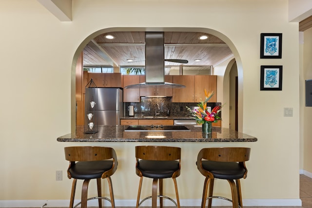 280 100th St, Ocean, Marathon, FL 33050 - kitchen with a breakfast bar area, brown cabinetry, stainless steel appliances, decorative backsplash, and island exhaust hood