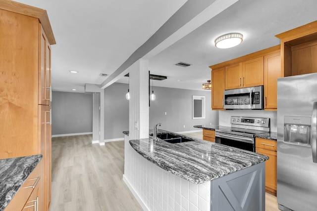 kitchen featuring baseboards, dark stone countertops, appliances with stainless steel finishes, light wood-style flooring, and a sink