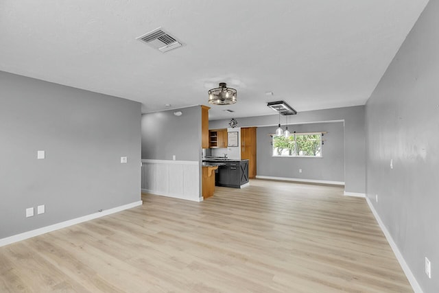 unfurnished living room with light wood-type flooring, visible vents, baseboards, and a sink