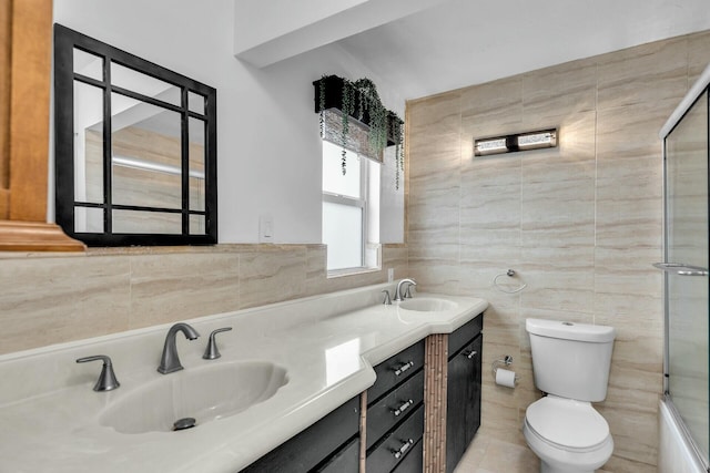 full bathroom featuring a shower with shower door, toilet, a sink, tile walls, and double vanity