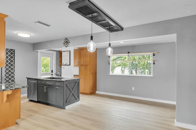 kitchen with a sink, dark stone counters, light wood-style floors, baseboards, and hanging light fixtures