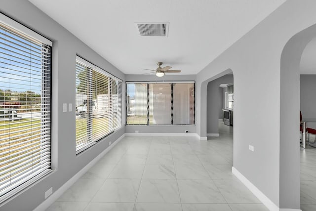 empty room featuring arched walkways, baseboards, visible vents, a ceiling fan, and marble finish floor