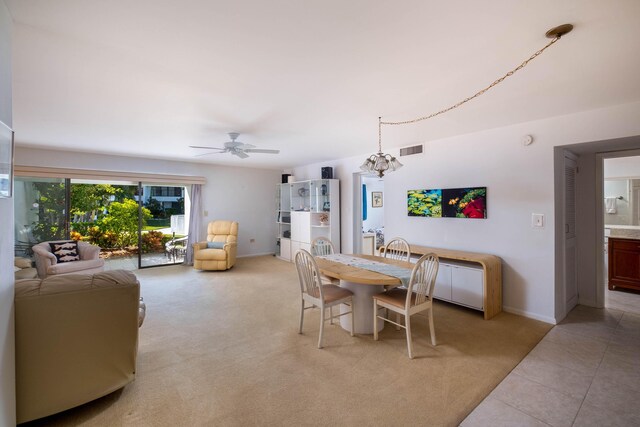 dining space featuring light tile patterned flooring, light colored carpet, ceiling fan with notable chandelier, visible vents, and baseboards