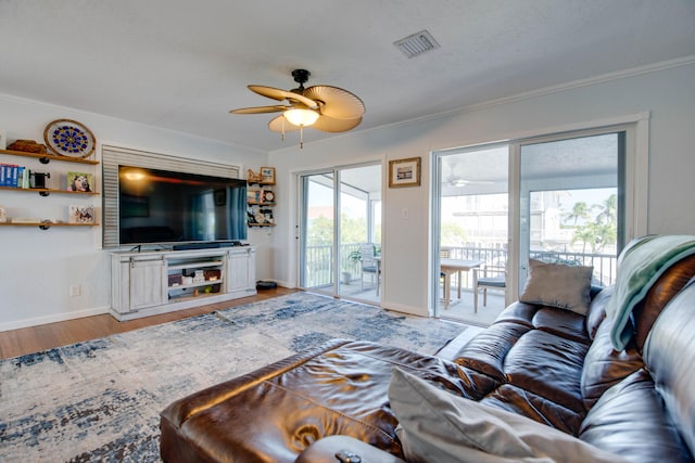 living area with ceiling fan, visible vents, wood finished floors, and ornamental molding