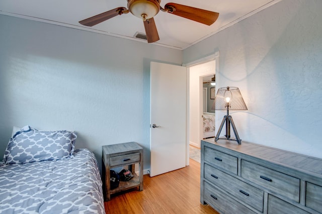 bedroom with crown molding, visible vents, a textured wall, light wood-style floors, and ceiling fan