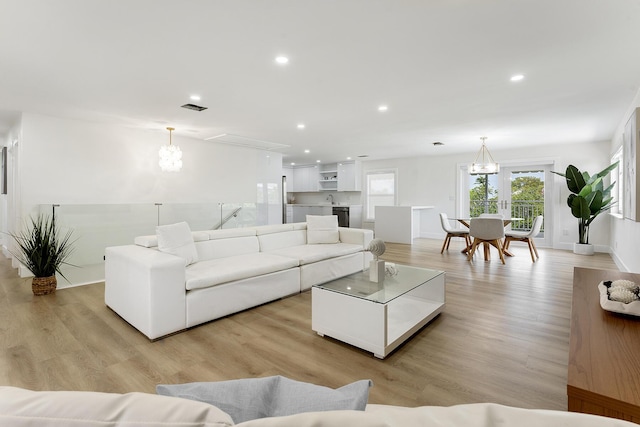 living area featuring visible vents, baseboards, light wood-style flooring, a notable chandelier, and recessed lighting