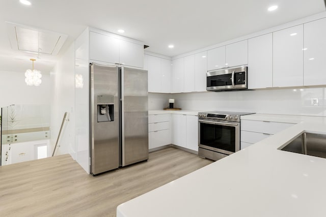 kitchen with appliances with stainless steel finishes, pendant lighting, light countertops, and white cabinets