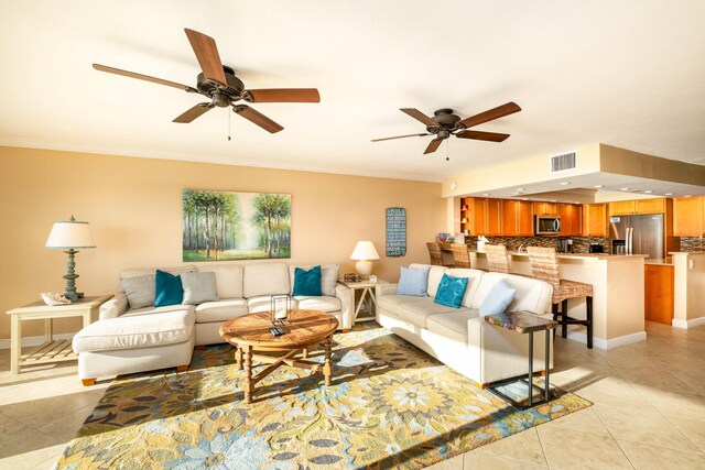 living area featuring light tile patterned floors, visible vents, baseboards, a ceiling fan, and crown molding