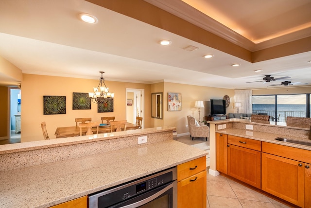 kitchen featuring light stone counters, open floor plan, ornamental molding, decorative light fixtures, and a sink