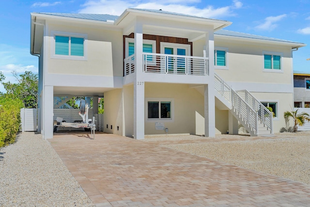 rear view of house featuring metal roof, stairs, decorative driveway, stucco siding, and a carport