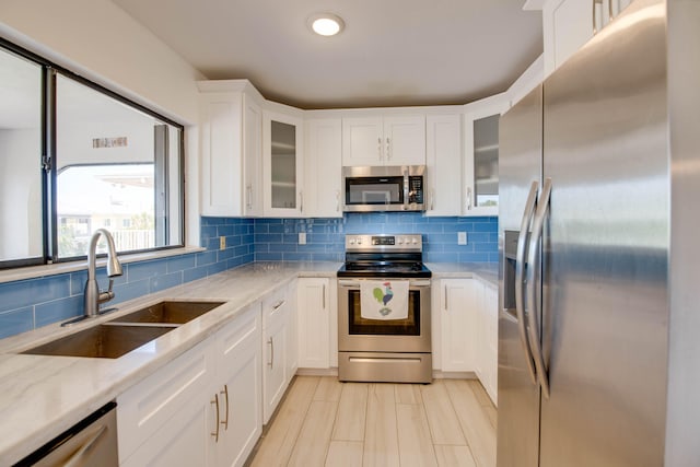 kitchen featuring a sink, white cabinetry, appliances with stainless steel finishes, light stone countertops, and glass insert cabinets