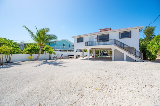 rear view of house featuring a carport, fence, driveway, and stairs