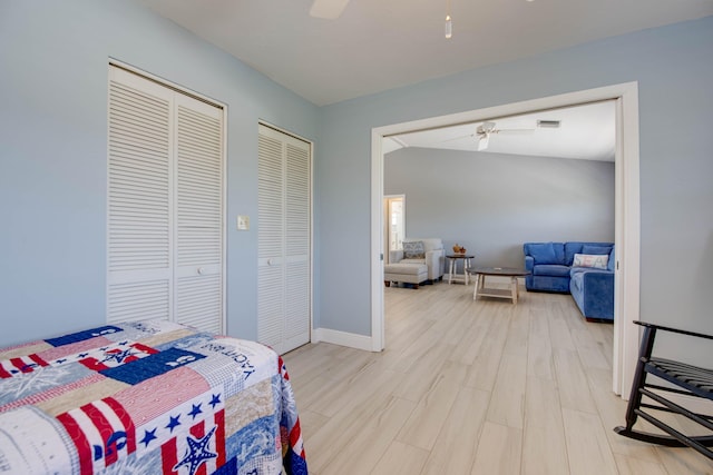 bedroom with wood finished floors, visible vents, baseboards, a ceiling fan, and two closets