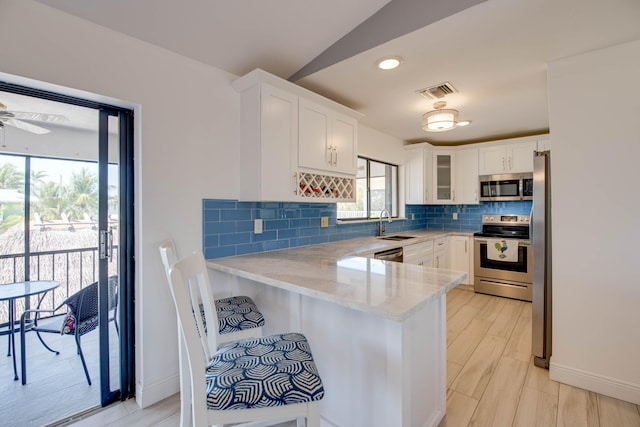 kitchen featuring glass insert cabinets, a peninsula, stainless steel appliances, white cabinetry, and backsplash