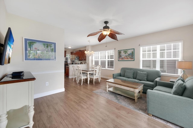 living room with ceiling fan with notable chandelier, light wood-type flooring, and baseboards