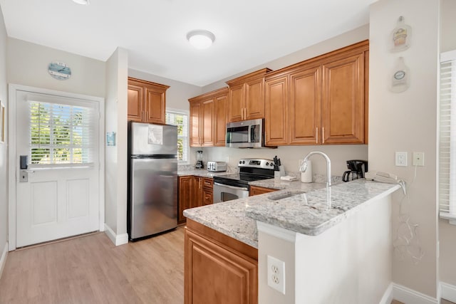 kitchen featuring brown cabinetry, appliances with stainless steel finishes, a peninsula, and a sink