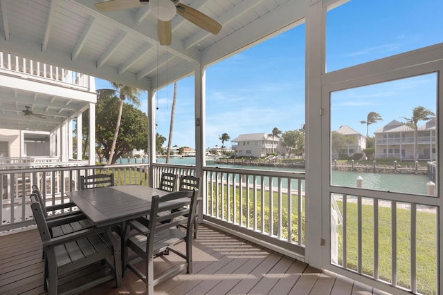 wooden deck featuring a water view, a lawn, outdoor dining space, and a ceiling fan