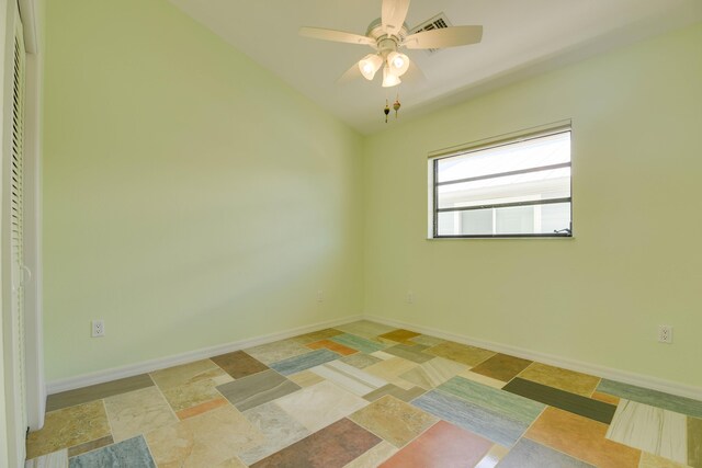 empty room with stone finish flooring, a ceiling fan, and baseboards