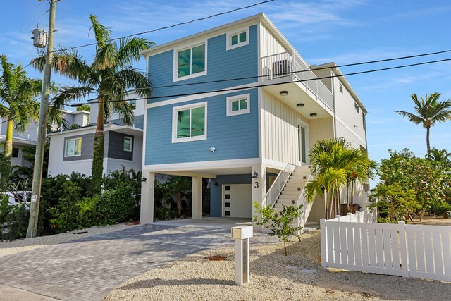 coastal inspired home with a carport, decorative driveway, fence, and stairs