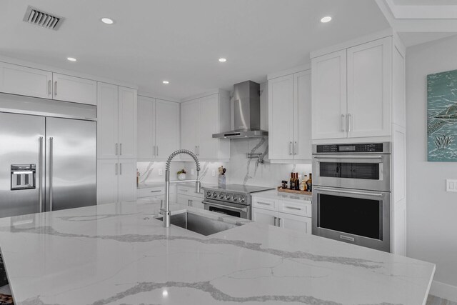 kitchen with high end appliances, white cabinets, visible vents, and wall chimney range hood