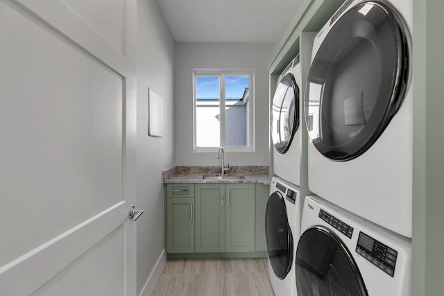 clothes washing area with stacked washer and dryer, a sink, cabinet space, and baseboards