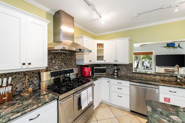 kitchen with glass insert cabinets, dark stone countertops, stainless steel appliances, wall chimney range hood, and white cabinetry