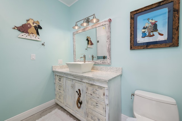 half bath featuring toilet, wood finished floors, vanity, and baseboards