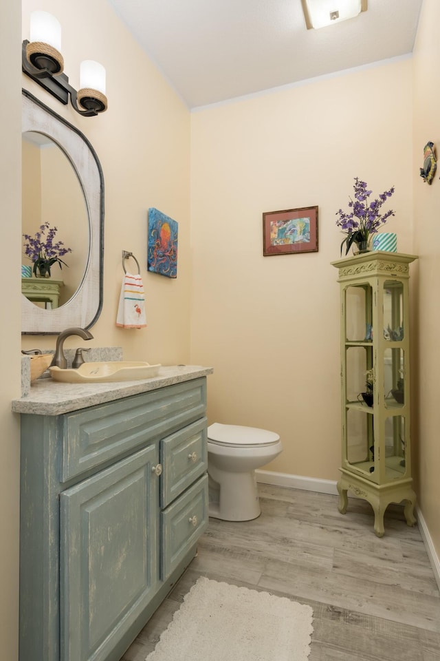 bathroom with toilet, baseboards, wood finished floors, and vanity