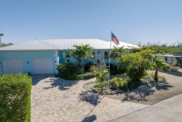 view of front facade with a garage, decorative driveway, metal roof, and stucco siding