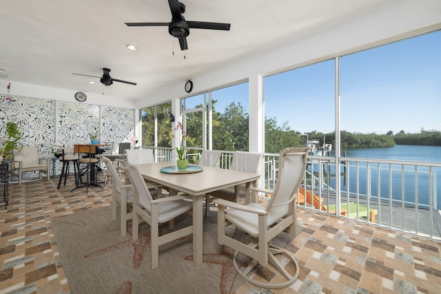 sunroom with plenty of natural light, a water view, and a ceiling fan