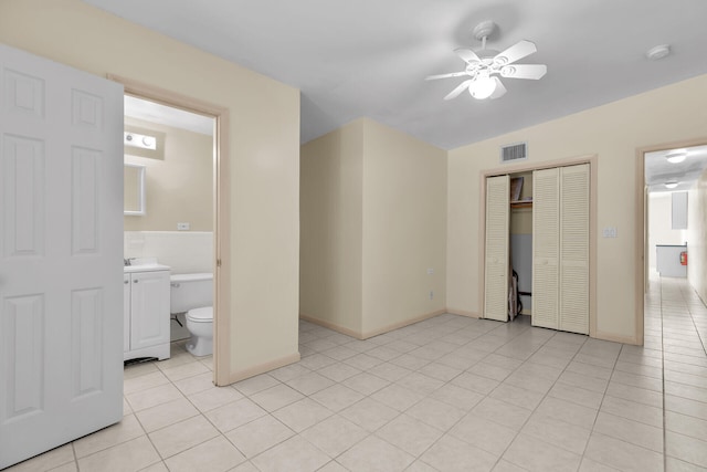 unfurnished bedroom with visible vents, a closet, ensuite bathroom, light tile patterned flooring, and a ceiling fan