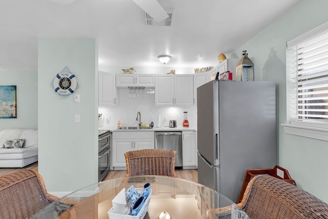 kitchen with a sink, visible vents, white cabinetry, light countertops, and appliances with stainless steel finishes