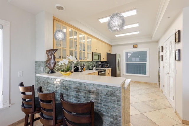 kitchen with appliances with stainless steel finishes, light countertops, decorative backsplash, a kitchen bar, and glass insert cabinets